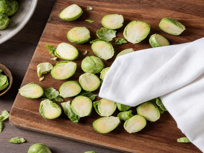 Halved Brussels sprouts being patted dry with a kitchen towel on a board