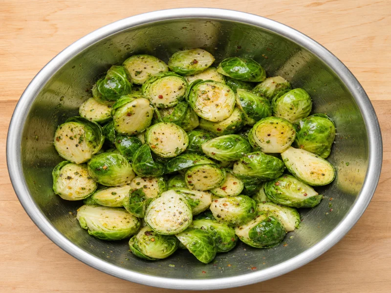 Brussels sprouts tossed in olive oil and seasonings in a stainless steel bowl