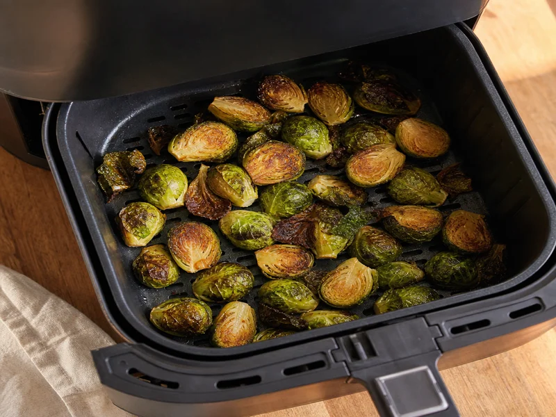 Golden-brown caramelized Brussels sprouts halfway through air frying with crispy outer leaves