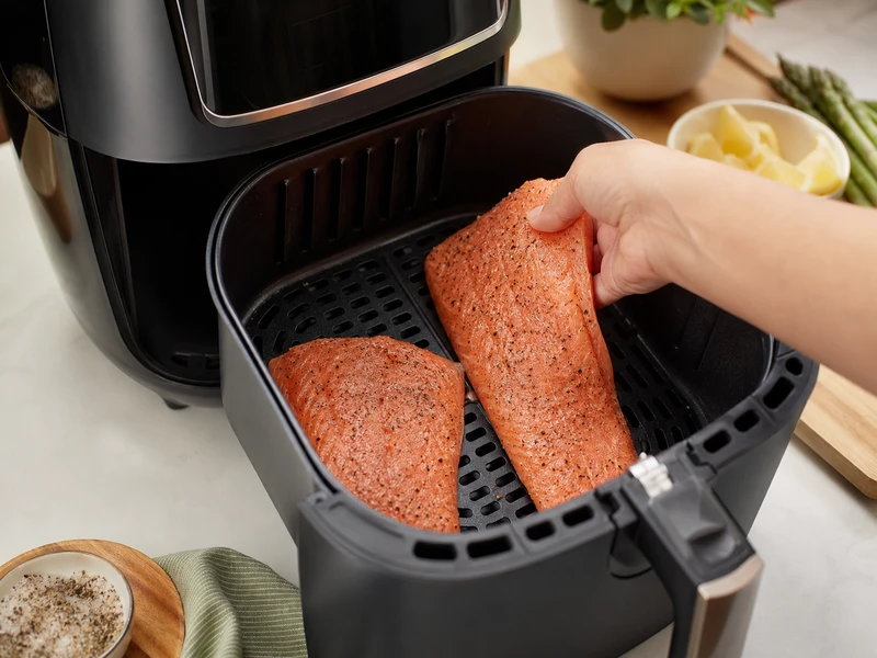 Placing seasoned salmon fillets in preheated air fryer basket