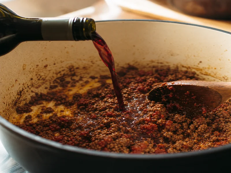 Ground beef browning with tomato paste and red wine in a pot
