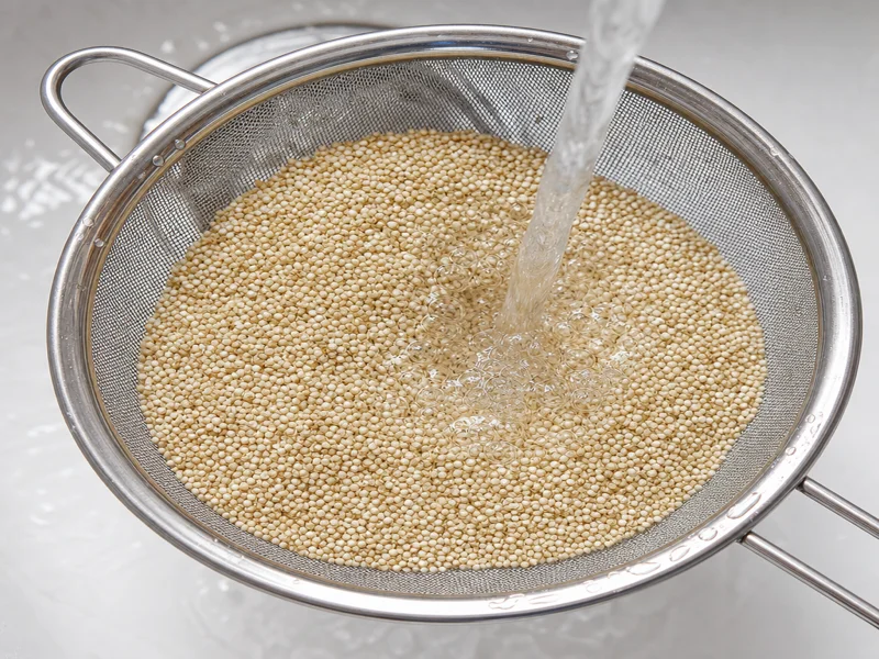 Rinsing white quinoa in a fine-mesh sieve under running water