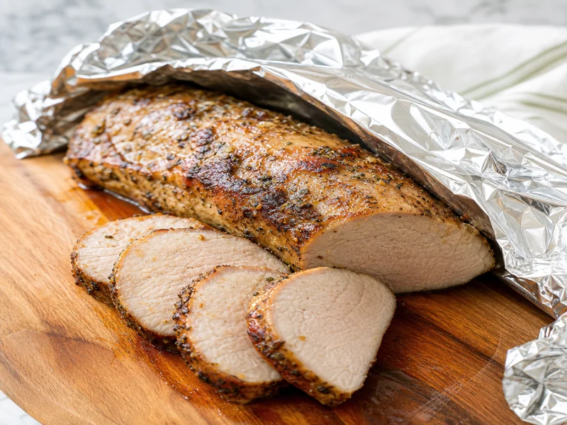 Roasted pork tenderloin resting under foil on a cutting board