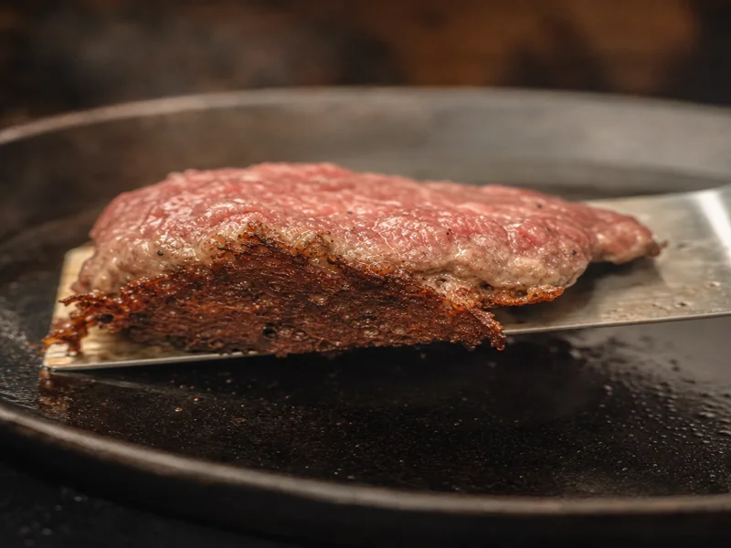 Flipping a smash burger patty showing a deeply browned crispy crust on the cooked side